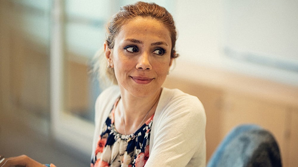 A female UX design employee seated at her workstation is smiling and looking to her left.