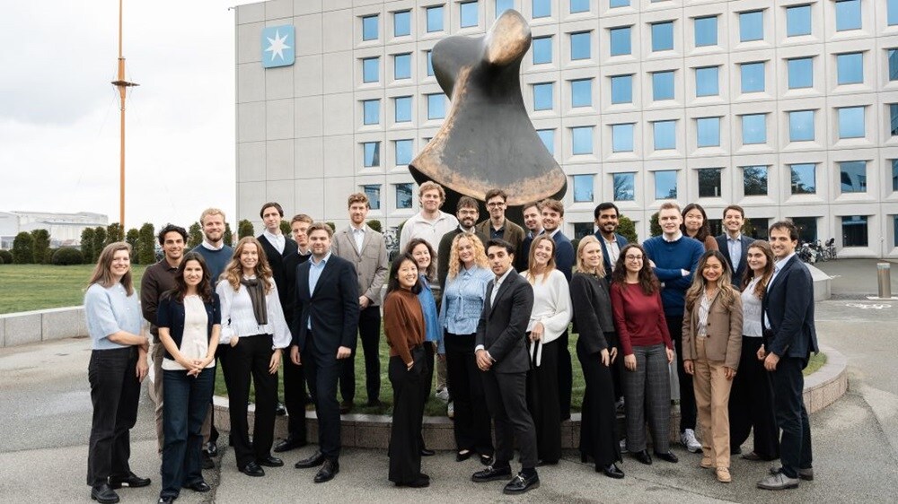 Large group of colleagues standing together outdoors in front of a modern office building and a large abstract sculpture.