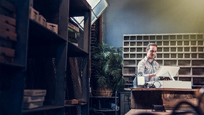 A man at an office desk, engaged in work with a laptop and documents spread out in front of him.