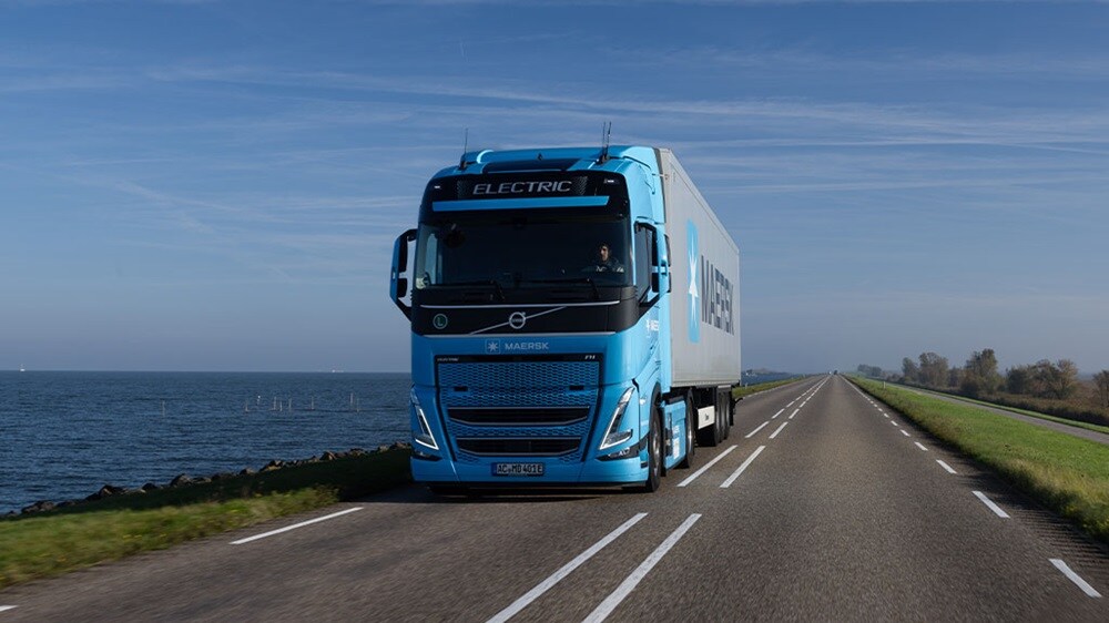 Electric Maersk truck driving on a coastal highway under a clear sky.