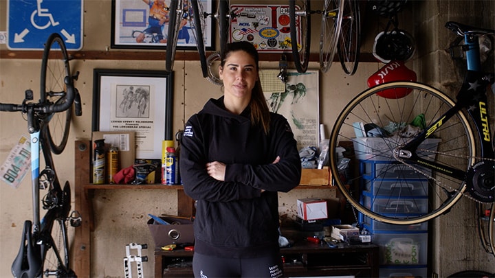 Mandy Marquardt, eine Sprint-Radfahrerin, mit Fahrradausrüstung im Hintergrund.